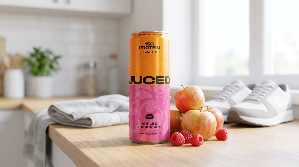 A can of JUCED Cloudy Apple & Raspberry protein drink beside fresh apples and raspberries on a bright kitchen counter, representing a high protein, low calorie drink option in the UK