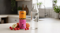 Can of JUCED Cloudy Apple and Raspberry protein drink beside a clear glass bottle of water, contrasting real fruit with a filtered clear format