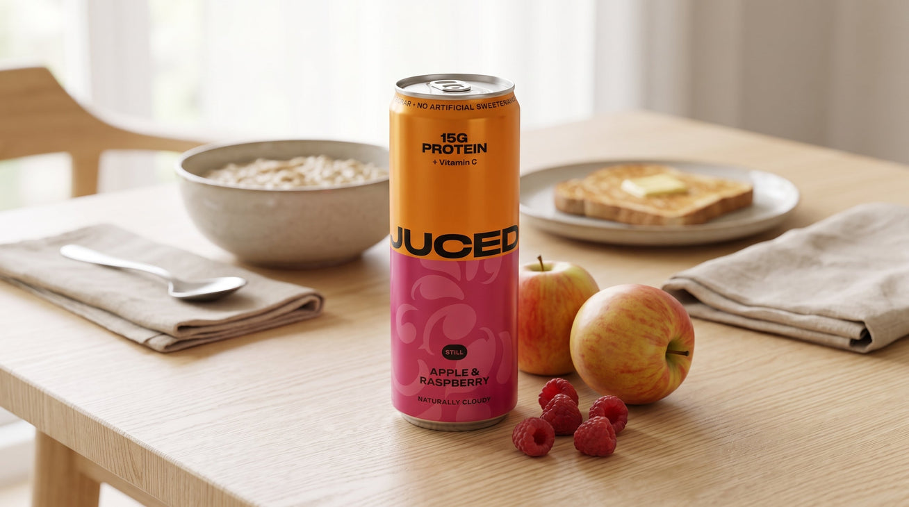 Can of JUCED Cloudy Apple and Raspberry protein drink on a breakfast table beside a bowl of porridge, toast and fresh apples and raspberries