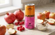 Cans of JUCED low sugar high protein drink next to fresh fruit on a kitchen counter