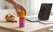 Person grabbing a can of JUCED Cloudy Apple and Raspberry protein drink from a desk while working, showing an easy way to get more protein during a busy day