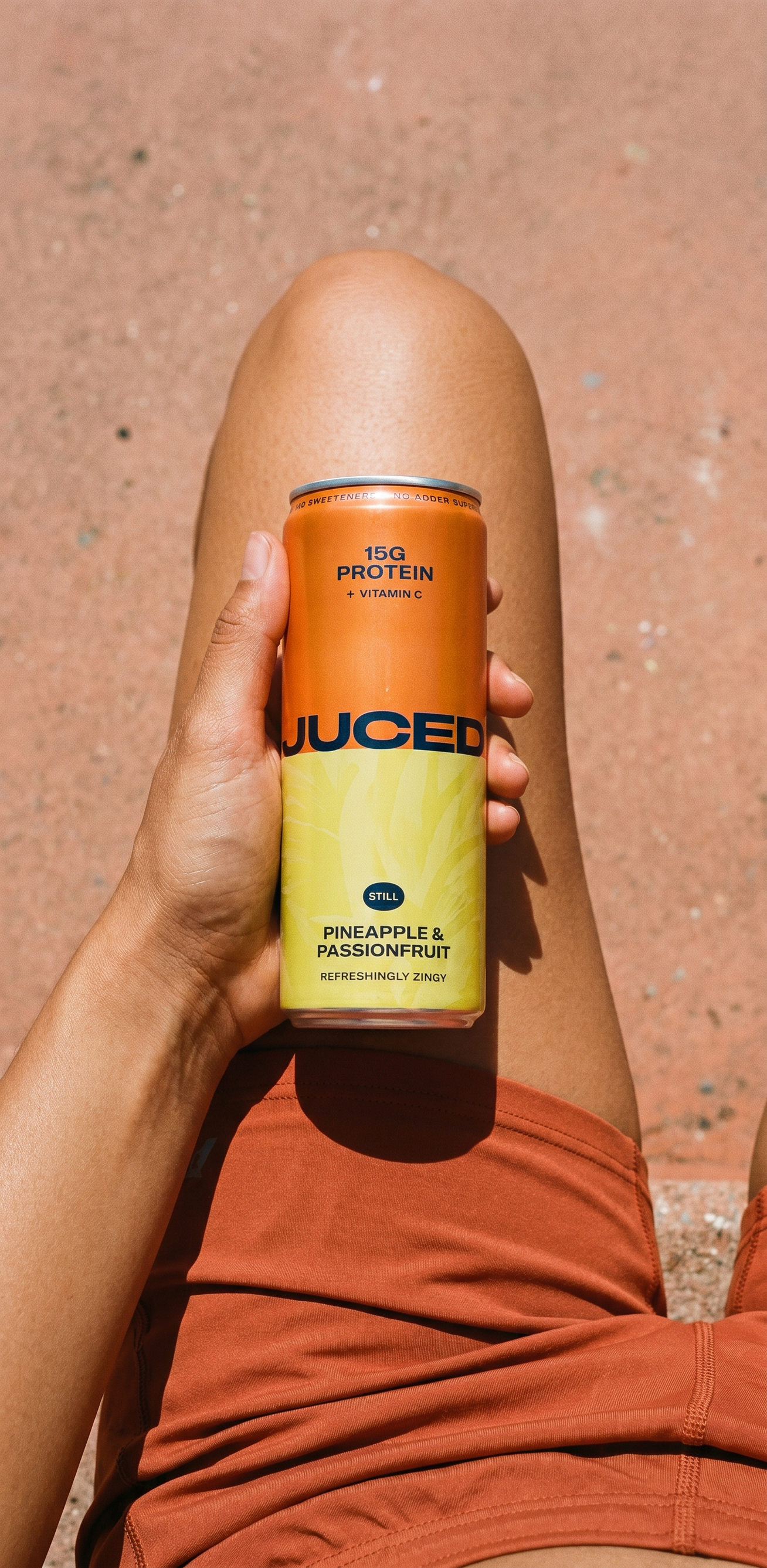 A chilled can of JUCED Pineapple and Passionfruit protein drink on a sunny outdoor table with fresh fruit